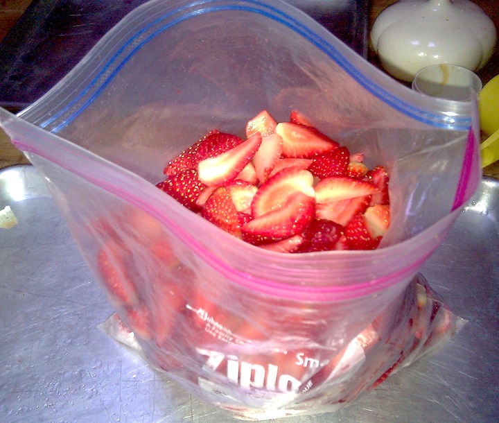 Cut up strawberries being put into a zippered ziplock bag.